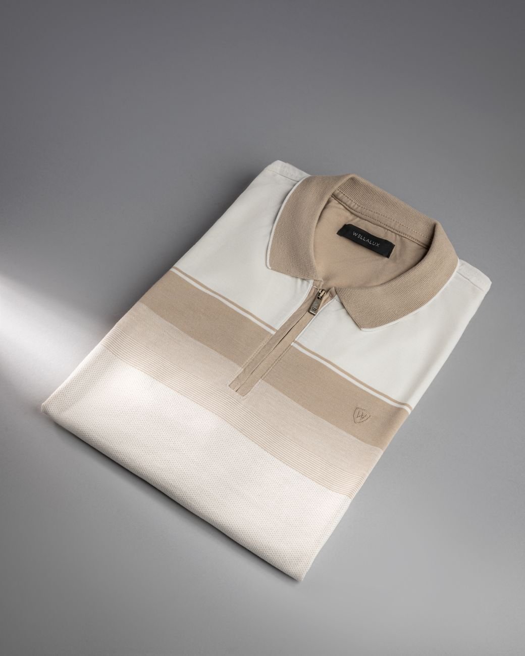 Stylish folded polo shirt in neutral tones on a gray studio background