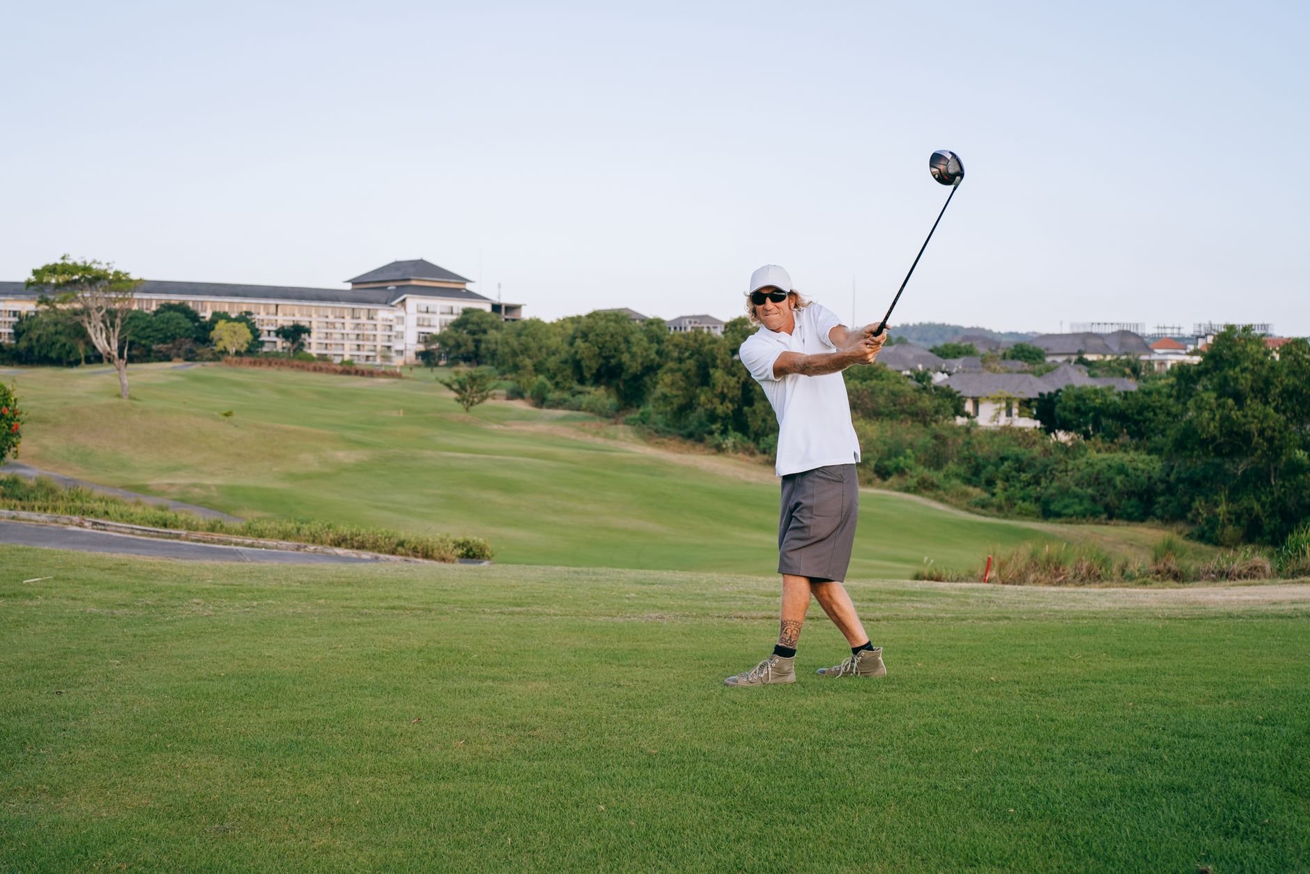 A golfer swings his club on a lush green course
